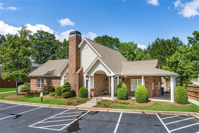 view of front of home with a front yard, uncovered parking, brick siding, and a chimney