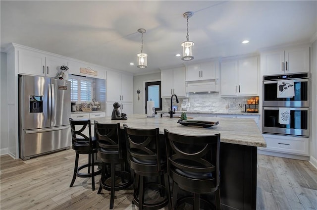 kitchen featuring white cabinets, appliances with stainless steel finishes, a sink, light wood finished floors, and decorative backsplash
