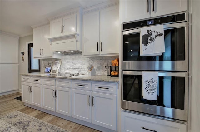 kitchen with decorative backsplash, crown molding, black electric cooktop, white cabinets, and double oven
