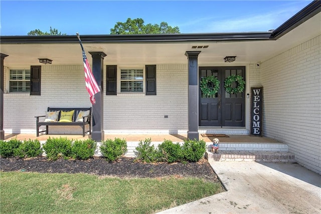 entrance to property featuring a porch and brick siding
