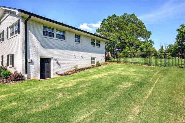 back of property featuring a lawn, fence, and brick siding