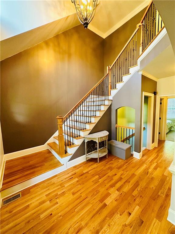 stairway featuring wood finished floors, visible vents, baseboards, a towering ceiling, and crown molding