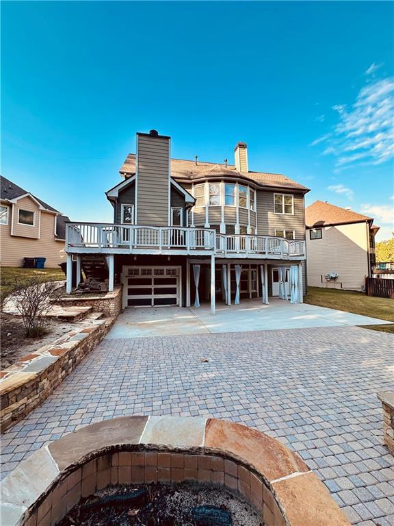 back of house with a wooden deck, a chimney, decorative driveway, and a garage