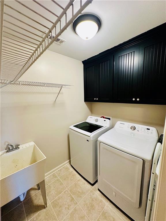 clothes washing area featuring a sink, cabinet space, separate washer and dryer, light tile patterned flooring, and baseboards