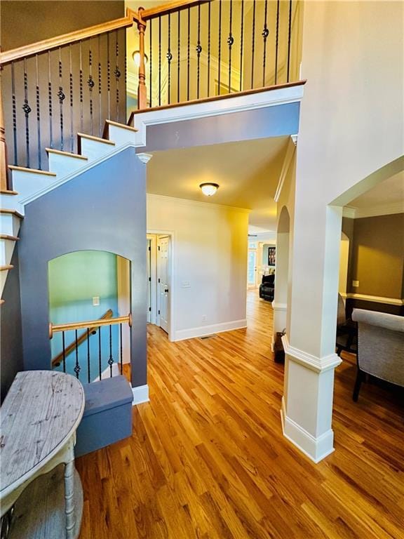 interior space featuring wood finished floors, arched walkways, baseboards, a towering ceiling, and stairs