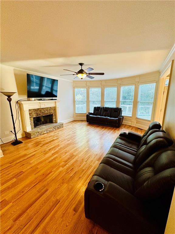 living room featuring crown molding, baseboards, a fireplace, wood finished floors, and a ceiling fan