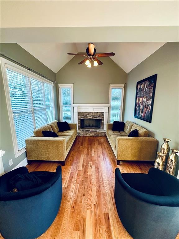 living room with lofted ceiling, a fireplace, light wood-type flooring, and ceiling fan