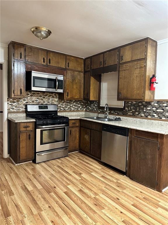 kitchen with appliances with stainless steel finishes, sink, ornamental molding, light hardwood / wood-style floors, and dark brown cabinetry