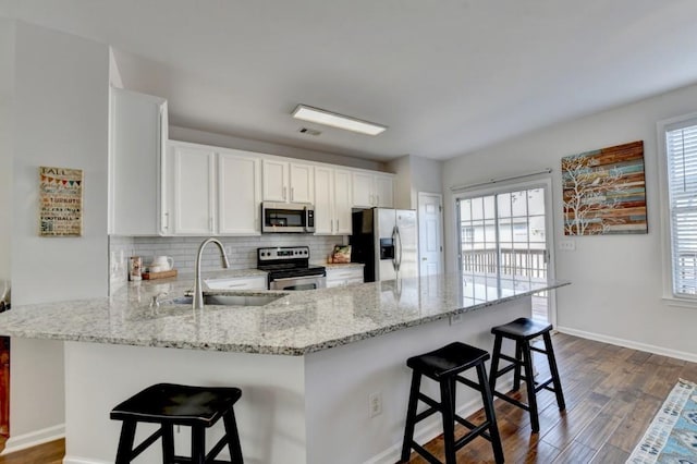 kitchen with a kitchen bar, appliances with stainless steel finishes, kitchen peninsula, and a wealth of natural light