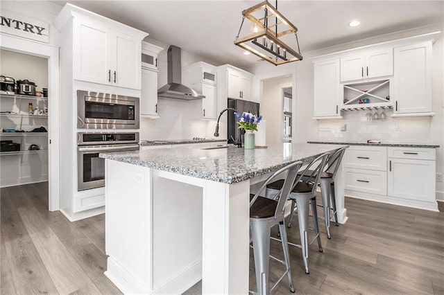 kitchen featuring white cabinets, wall chimney range hood, stainless steel appliances, sink, and a kitchen island with sink