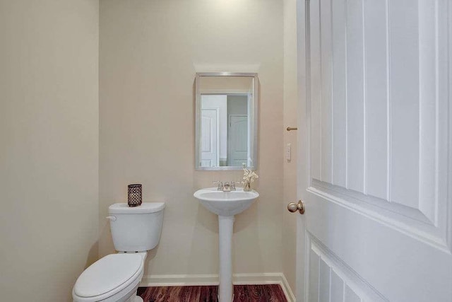 half bathroom featuring wood finished floors, toilet, and baseboards