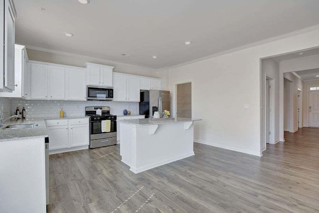 kitchen featuring stainless steel appliances, a kitchen island, a sink, backsplash, and light wood finished floors