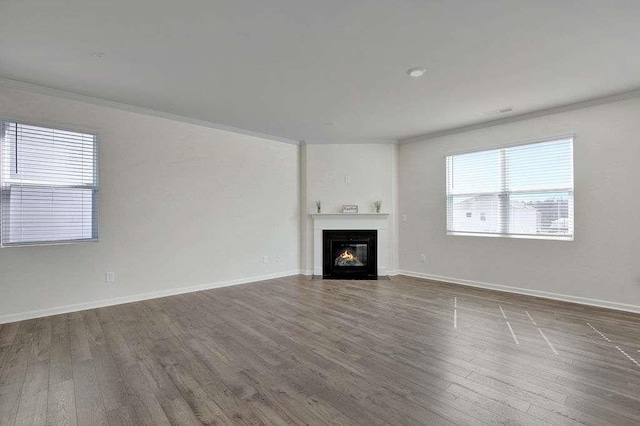 unfurnished living room with wood finished floors, visible vents, baseboards, a lit fireplace, and ornamental molding