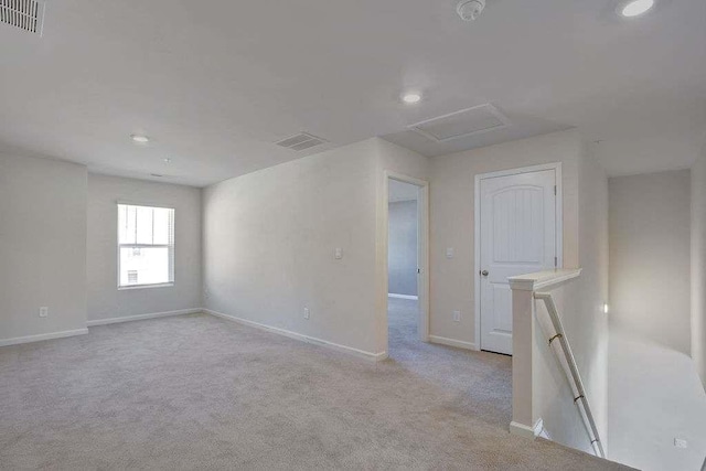 empty room featuring light carpet, attic access, visible vents, and baseboards