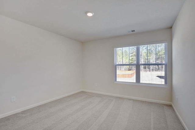 spare room featuring light colored carpet, visible vents, and baseboards