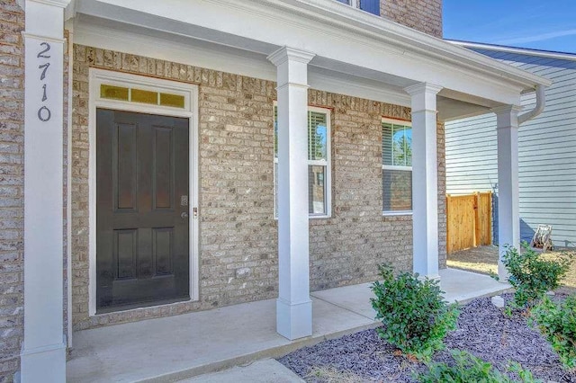 doorway to property featuring a porch and brick siding