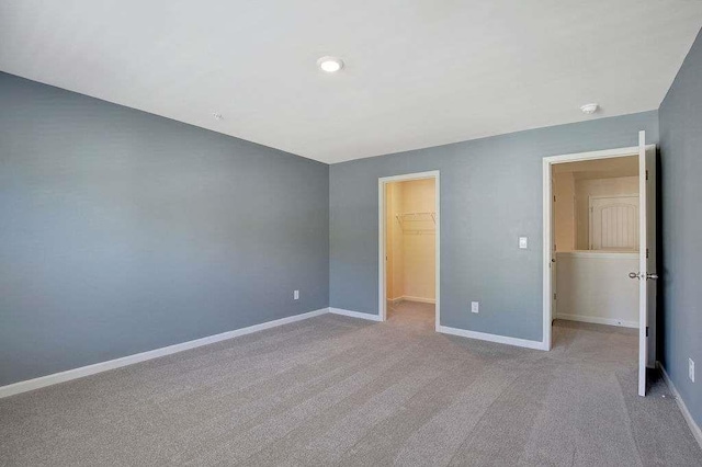 unfurnished bedroom featuring a closet, a walk in closet, carpet, and baseboards