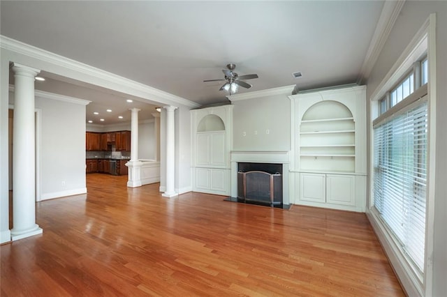 unfurnished living room featuring a ceiling fan, a fireplace, decorative columns, light wood-type flooring, and ornamental molding