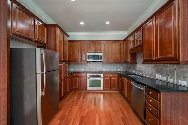 kitchen with appliances with stainless steel finishes, a sink, crown molding, light wood-type flooring, and glass insert cabinets
