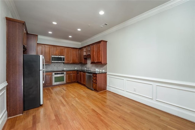 kitchen with appliances with stainless steel finishes, ornamental molding, dark countertops, light wood-style floors, and decorative backsplash