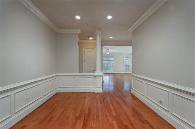 corridor featuring decorative columns, crown molding, a decorative wall, light wood-style flooring, and recessed lighting