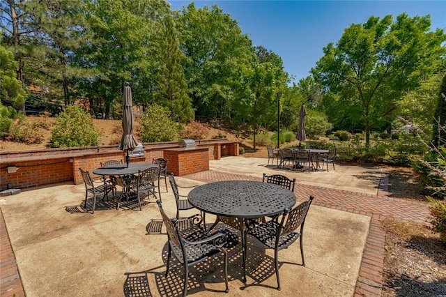 view of patio / terrace featuring outdoor dining space, view of wooded area, and exterior kitchen
