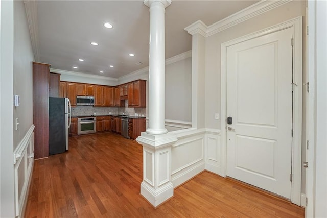 kitchen featuring stainless steel appliances, ornate columns, crown molding, brown cabinets, and wood finished floors