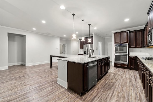 kitchen with sink, decorative light fixtures, a center island with sink, stainless steel appliances, and light stone countertops