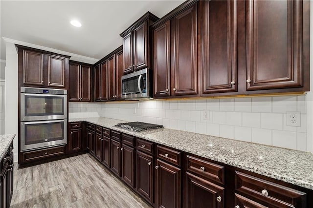 kitchen featuring light stone counters, backsplash, stainless steel appliances, and light wood-type flooring