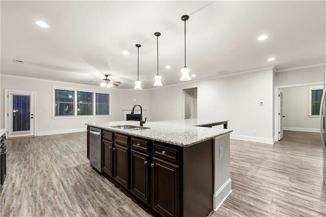 kitchen featuring decorative light fixtures, sink, light stone counters, a center island with sink, and light wood-type flooring