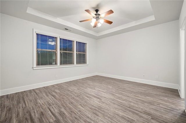 empty room featuring dark hardwood / wood-style flooring, a raised ceiling, and ceiling fan