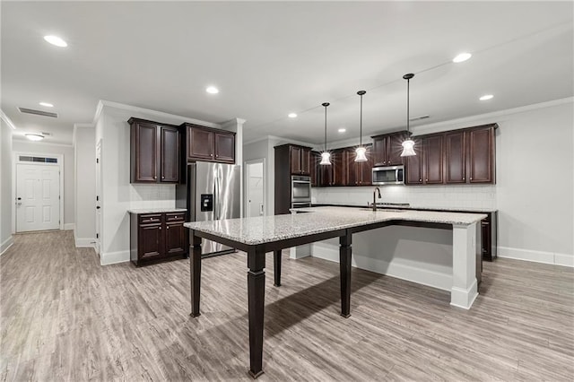 kitchen featuring hanging light fixtures, backsplash, stainless steel appliances, ornamental molding, and an island with sink