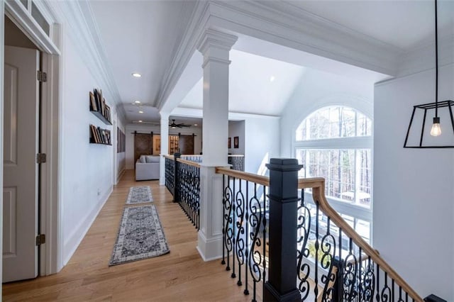 hallway featuring light wood-type flooring, ornamental molding, and ornate columns