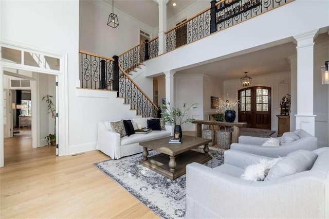 living room with a towering ceiling, decorative columns, hardwood / wood-style flooring, ornamental molding, and french doors