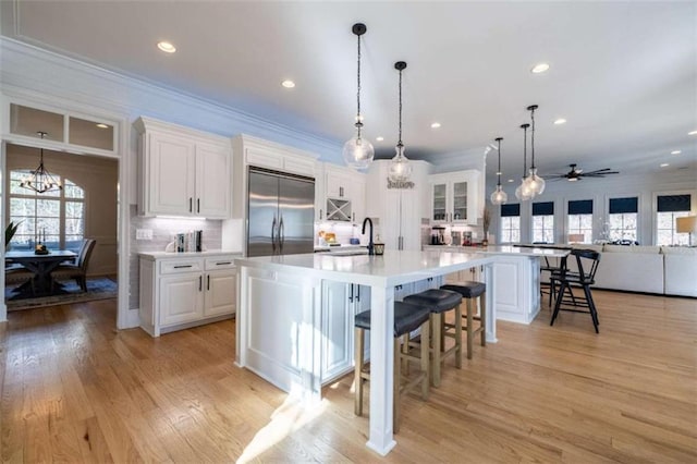 kitchen with sink, a breakfast bar area, white cabinets, built in fridge, and a large island with sink