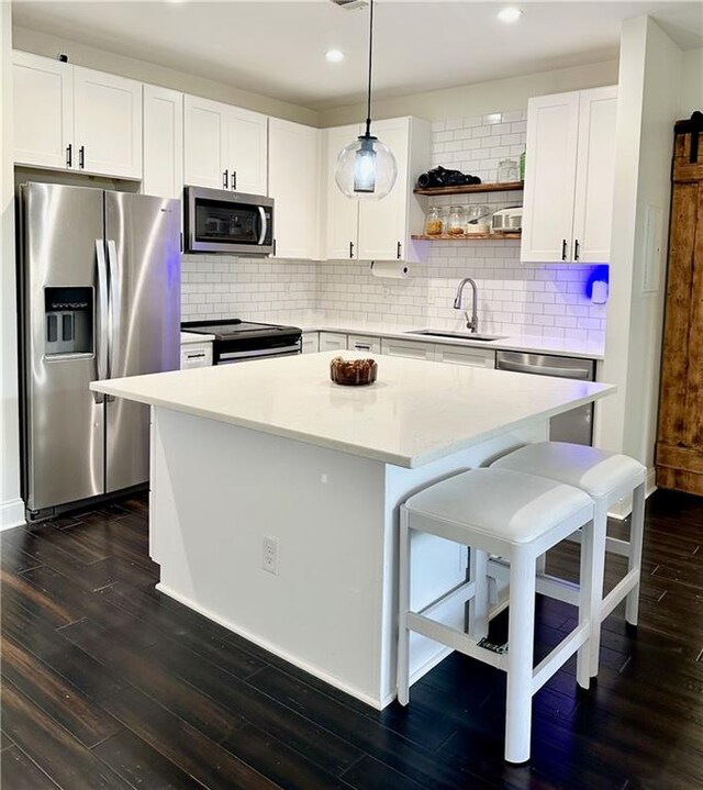 kitchen featuring appliances with stainless steel finishes, hanging light fixtures, white cabinetry, dark wood-type flooring, and sink