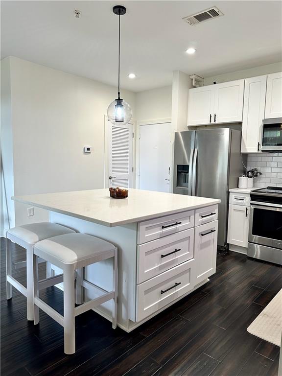 kitchen featuring white cabinets, appliances with stainless steel finishes, and hanging light fixtures