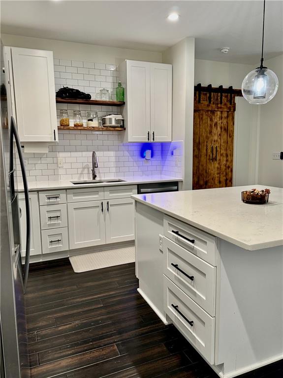 kitchen with white cabinetry, dark wood-type flooring, a barn door, backsplash, and sink