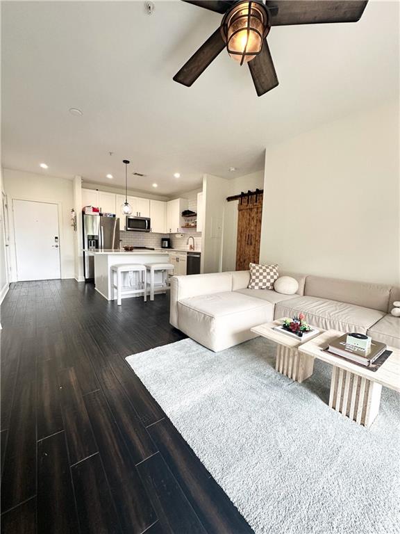 living room with a barn door, dark hardwood / wood-style floors, and ceiling fan