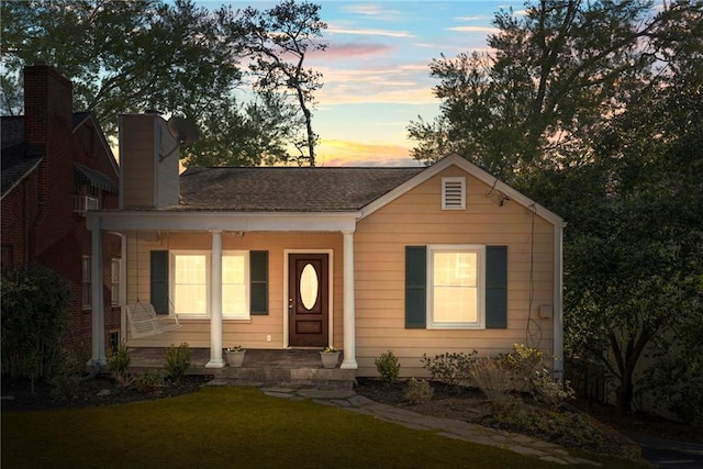 view of front of property featuring a front yard, covered porch, roof with shingles, and a chimney