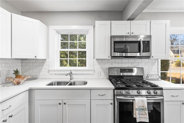 kitchen with decorative backsplash, white cabinets, appliances with stainless steel finishes, and a sink