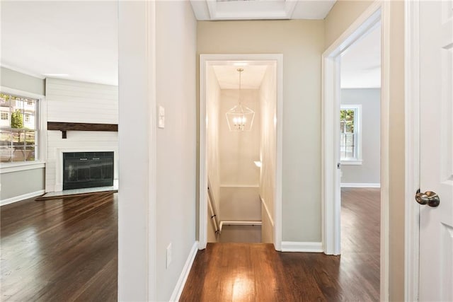 corridor with a notable chandelier, wood finished floors, and baseboards