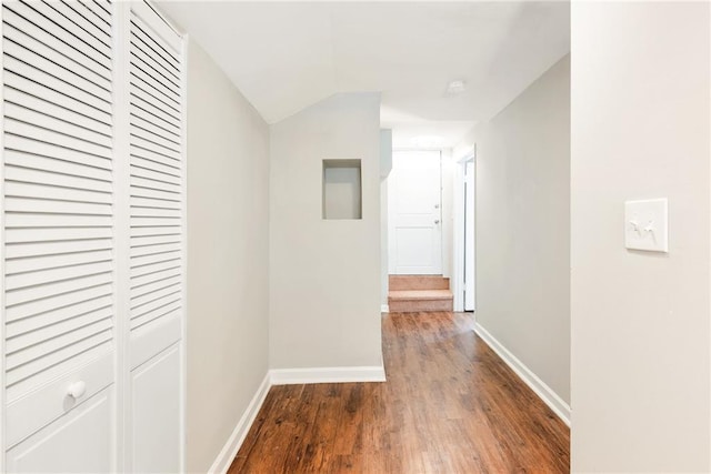 hallway featuring baseboards, wood finished floors, and vaulted ceiling