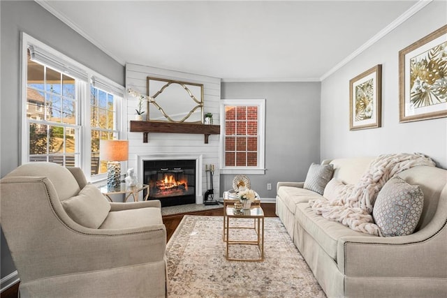 living room with baseboards, wood finished floors, a glass covered fireplace, and crown molding