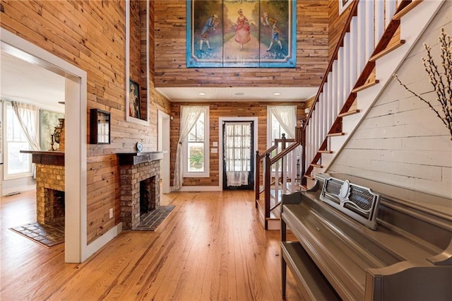 entryway featuring a fireplace, light wood finished floors, a high ceiling, wooden walls, and stairs