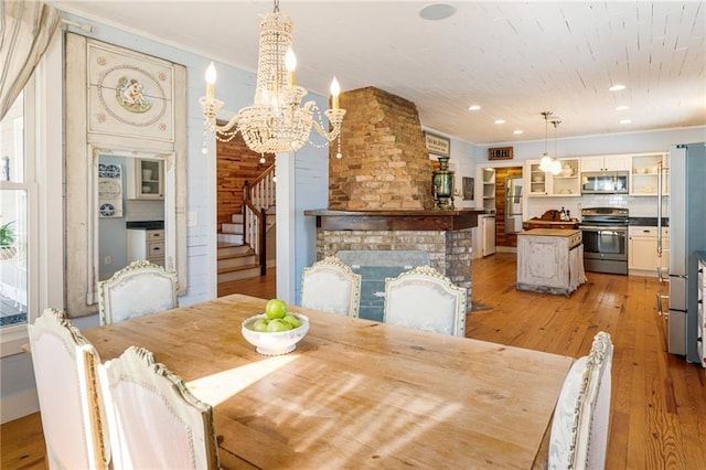 dining area featuring a fireplace, recessed lighting, stairway, light wood-style flooring, and a chandelier