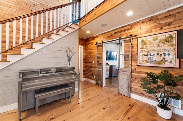 hallway with baseboards, a barn door, wood finished floors, and wooden walls