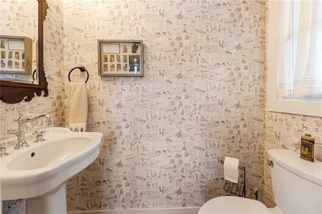 bathroom with toilet, wallpapered walls, and a sink