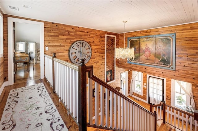 hallway with visible vents, wood walls, wood finished floors, and an upstairs landing