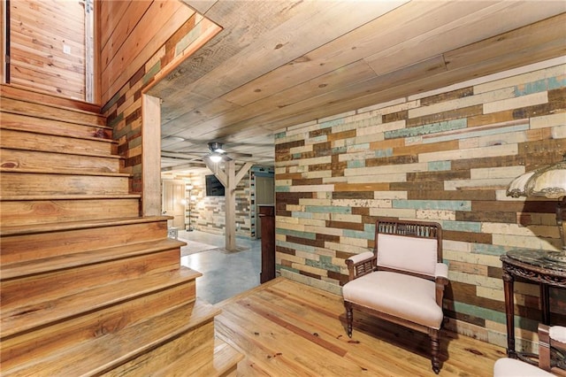 sitting room with wooden walls, wooden ceiling, ceiling fan, stairs, and concrete floors